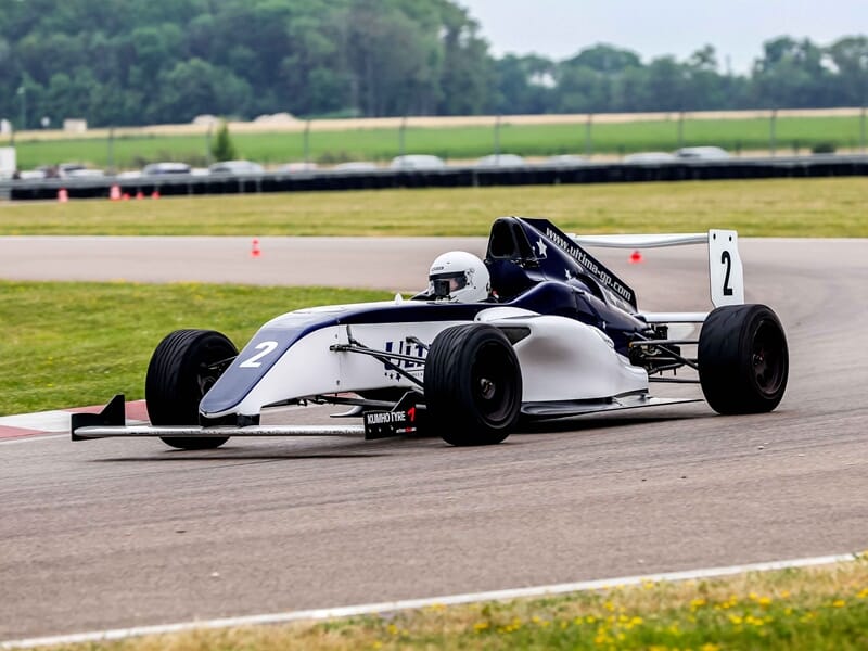 Formule 4 au circuit de Pont l'Evêque blanche et bleue numéro 2 prenant un virage