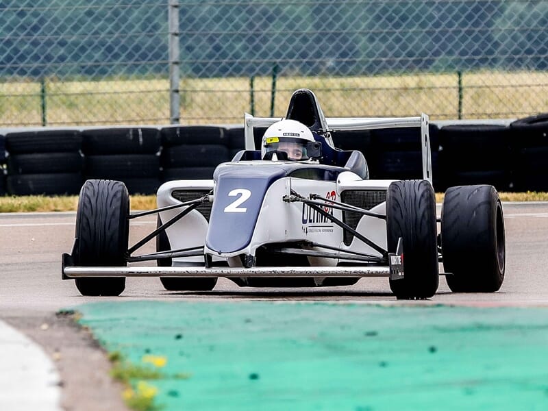 Formule 4 au circuit de Pont l'Evêque blanche et bleue vue de face sur piste avec pilote casqué concentré au volant.
