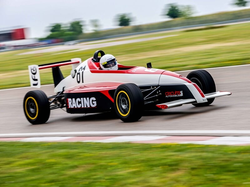 Formule Renault au circuit de Pont l'Evêque rouge et blanche en virage sur piste, pilote concentré avec casque blanc, ambiance de vitesse.
