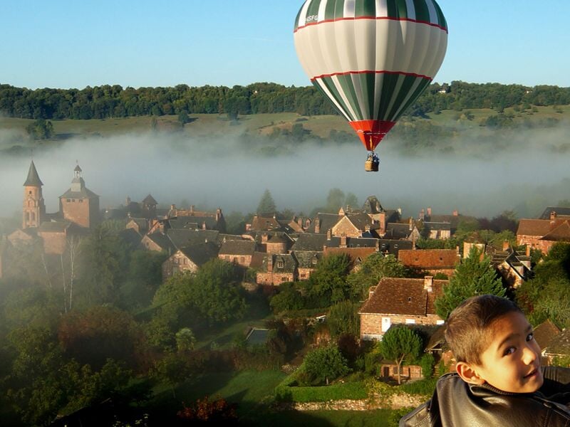 Montgolfière colorée volant au-dessus d'un village avec un enfant regardant vers la caméra.