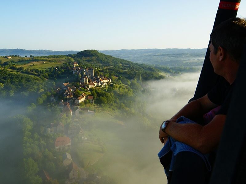 Vue depuis une montgolfière sur un paysage vallonné avec un homme regardant vers l'horizon.