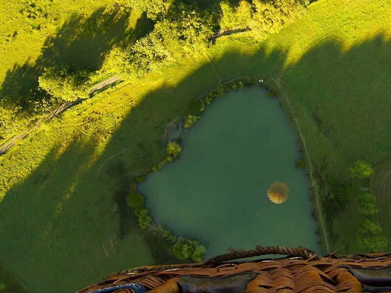 Vue aérienne depuis une montgolfière montrant un lac en forme de cœur entouré de verdure.