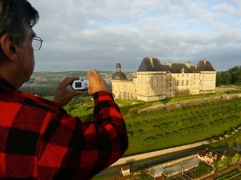 Homme en chemise à carreaux rouges prenant une photo d'un château depuis une montgolfière.