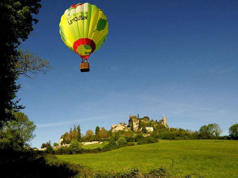 Montgolfière colorée volant au-dessus d'un village médiéval sur une colline verdoyante par ciel clair.
