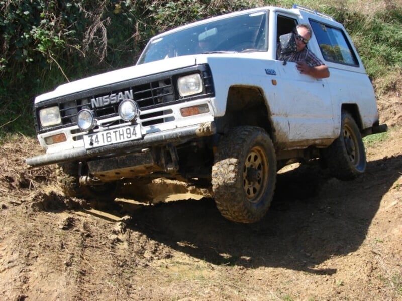4x4 blanc avec conducteur sortant la tête par la fenêtre sur un chemin boueux.