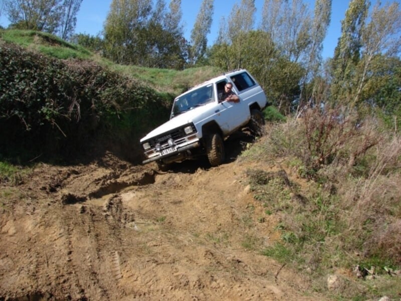 Même Nissan 4x4 descendant une forte pente terreuse, conducteur observant la trajectoire, végétation clairsemée en arrière-plan.