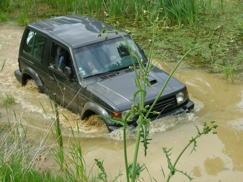 Jeep noire évoluant dans une zone sableuse avec végétation, terrain accidenté.