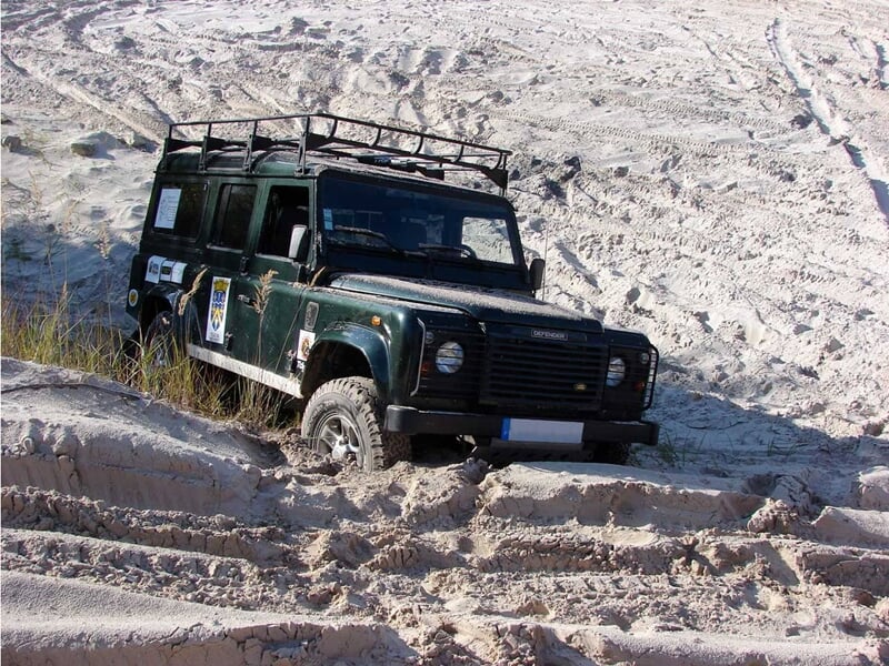 4x4 vert foncé roulant sur un chemin sablonneux avec des arbres en arrière-plan.
