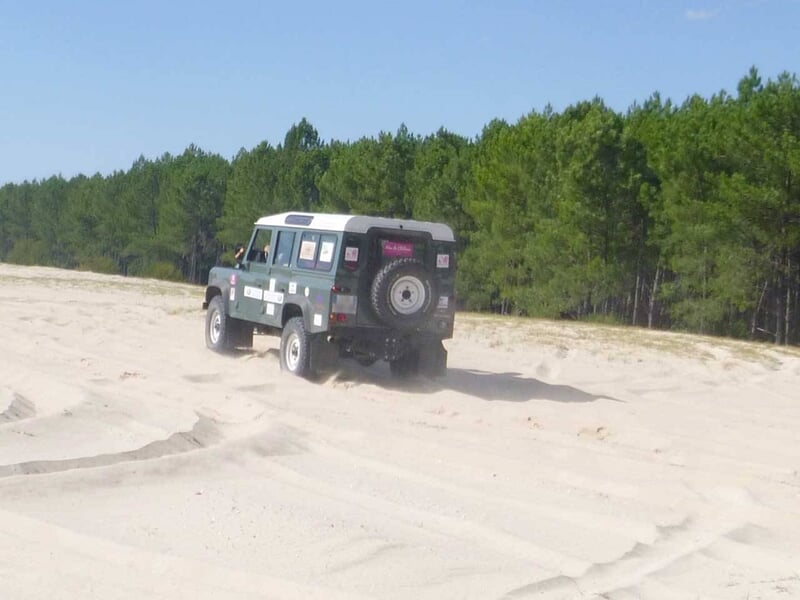 Jeep noire franchissant un obstacle rocheux sur un terrain sablonneux en forêt.