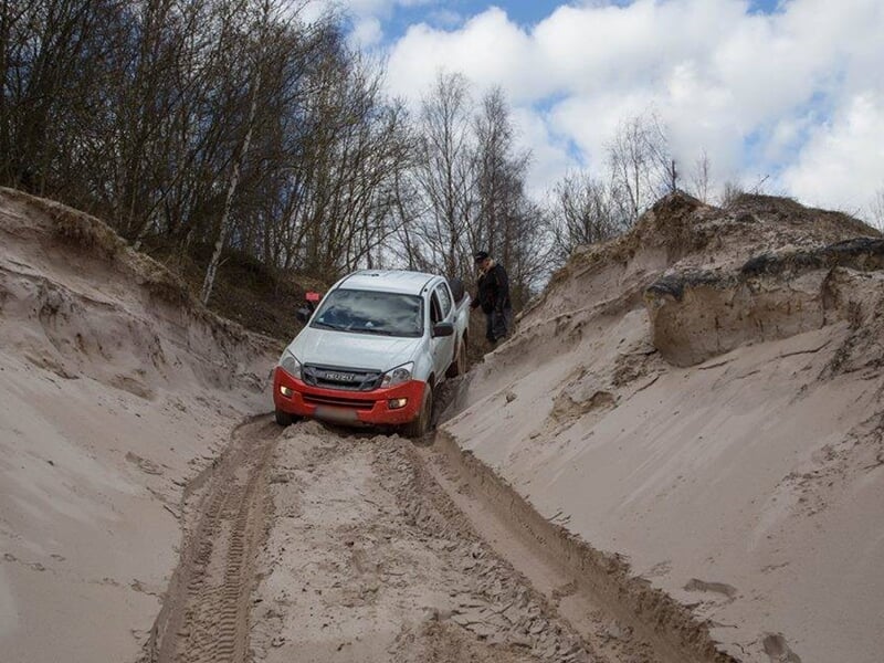 SUV rose et bleu franchissant un obstacle sur un terrain sablonneux avec arbres.