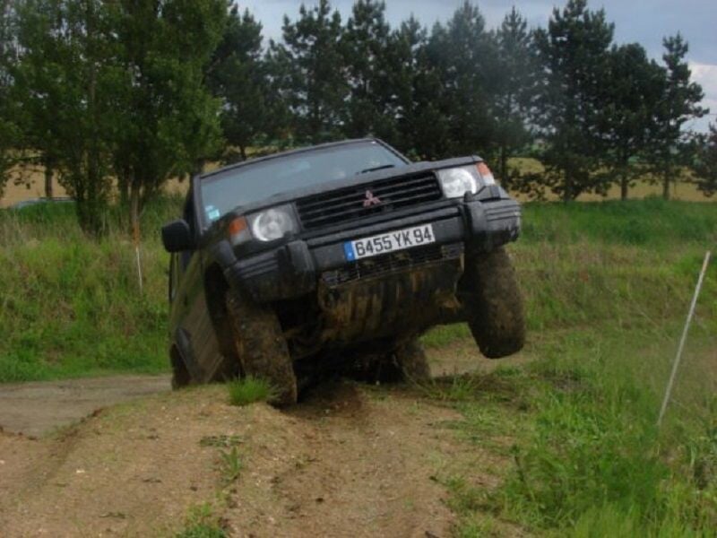 Véhicule 4x4 franchissant un obstacle en terrain boueux avec une roue avant levée en l'air.