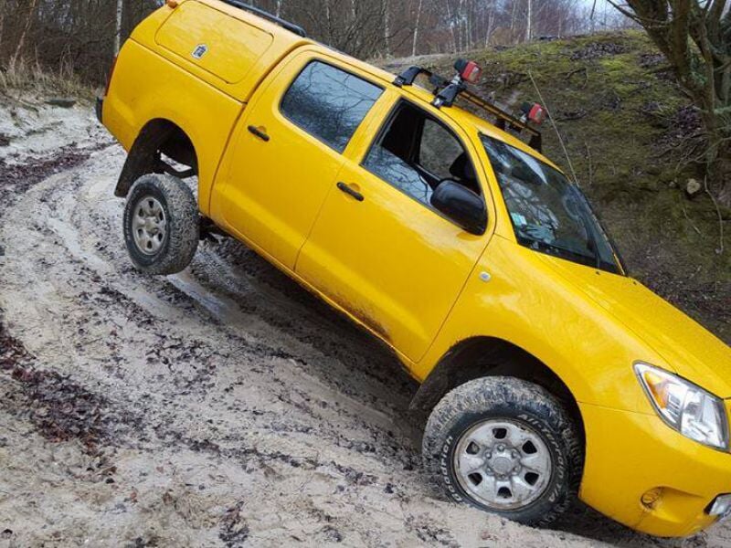 Pick-up jaune en montée sur un chemin boueux et glissant dans un environnement forestier.
