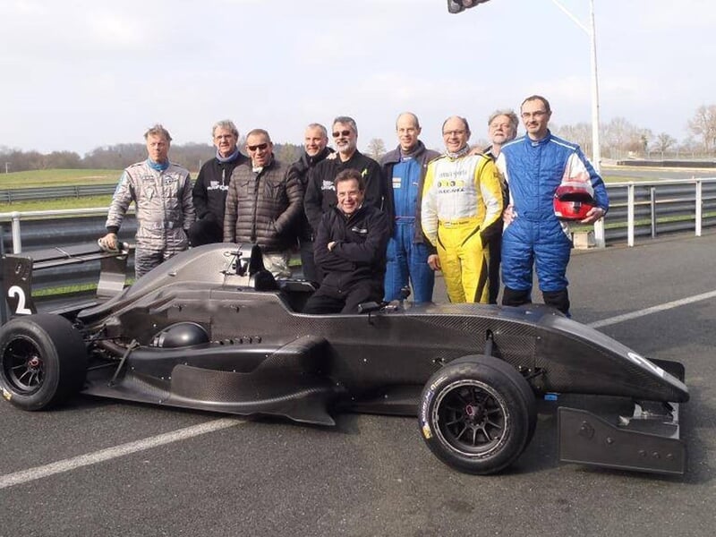 Groupe de pilotes posant derrière une monoplace noire sur la piste du circuit de La Châtre en Indre.