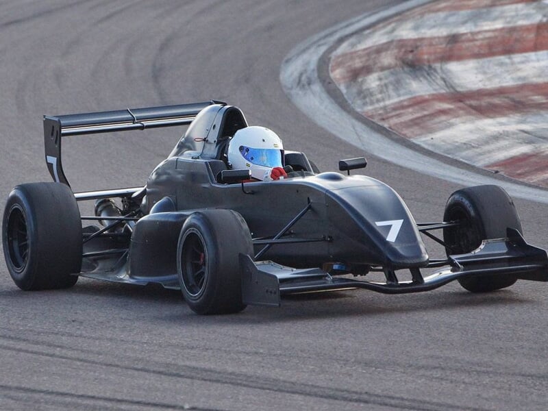 Monoplace noire numéro 7 avec pilote en casque blanc roulant sur la piste du circuit automobile.