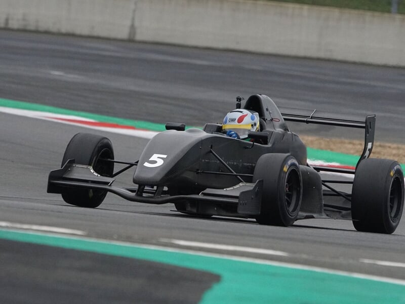 Monoplace noire numéro 5 avec pilote en casque blanc sur piste de course avec marquages verts.