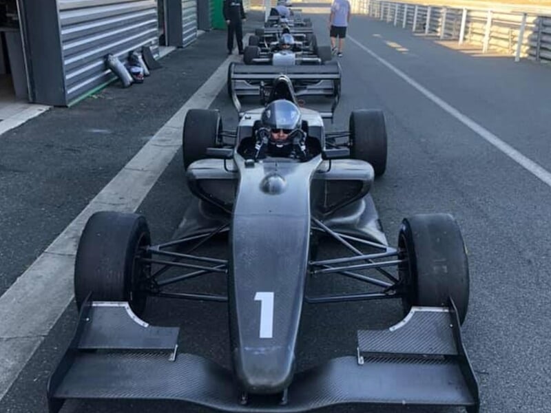 Pilote casqué assis dans une monoplace noire numéro 1 garée dans les stands du circuit.