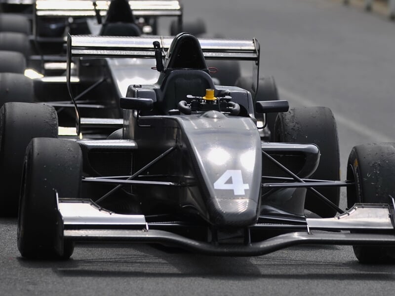 Monoplace noire numéro 4 roulant sur piste de course avec pilote casqué visible dans le cockpit.
