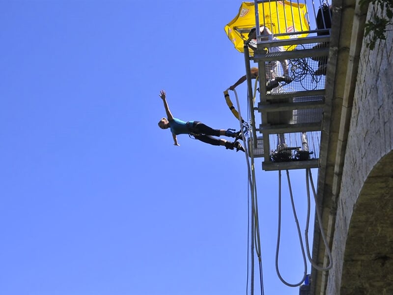 Une personne en position d'ange effectue un saut à l'élastique depuis une plateforme avec un parapluie jaune visible à côté.