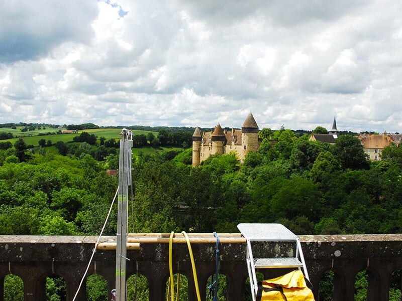 Vue sur un château entouré de verdure, prise depuis une plate-forme équipée pour le saut à l'élastique.