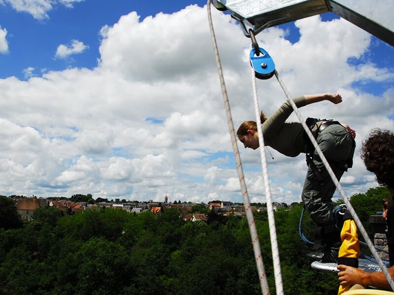 Une femme en position de saut à l'élastique, se penchant vers l'avant depuis une plate-forme, sous un ciel ensoleillé.
