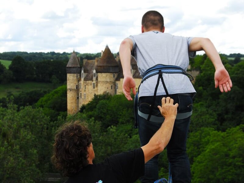 Un homme prêt à sauter à l'élastique, avec un instructeur l'accompagnant, et un château en arrière-plan.