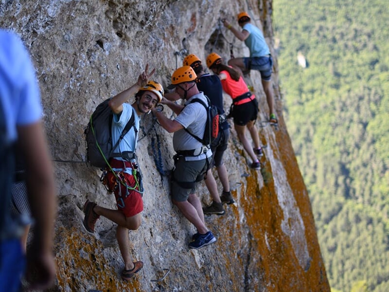 Groupe de grimpeurs accrochés à une paroi rocheuse, formant une file, avec certains posant pour la photo tout en souriant.