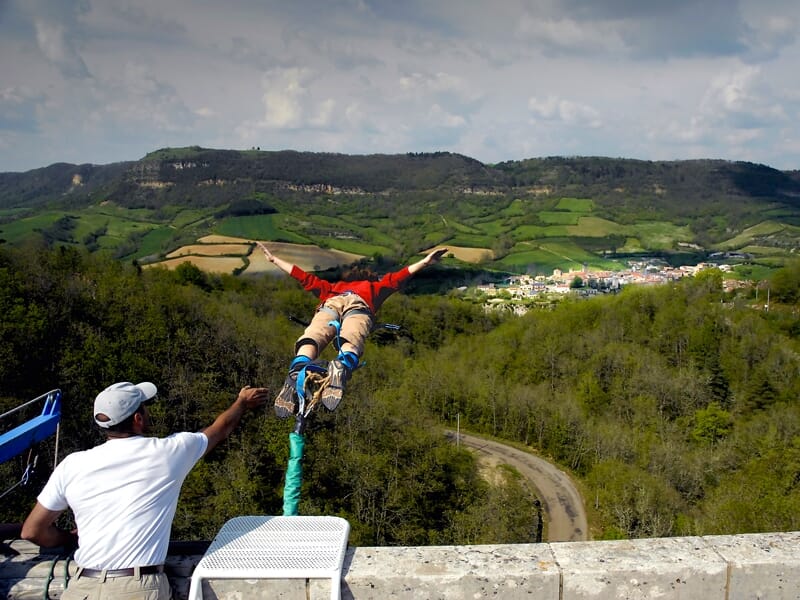 Personne en combinaison rouge effectuant un saut à l'élastique au-dessus d'un paysage vallonné et verdoyant.