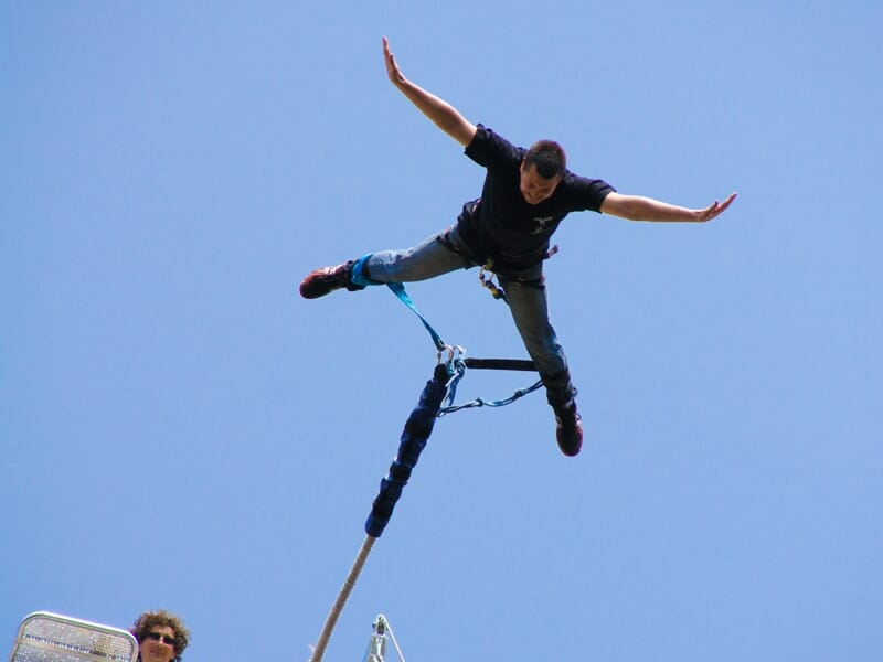 Homme effectuant un saut à l'élastique avec les bras écartés, suspendu dans le ciel bleu sans nuages.