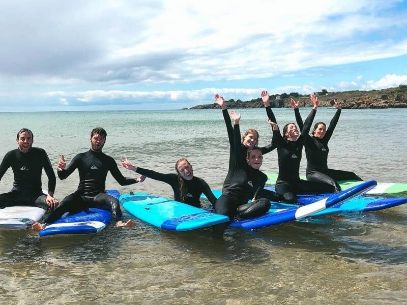 Un groupe d'élèves assis sur leurs planches de surf côte à côte et joyeux