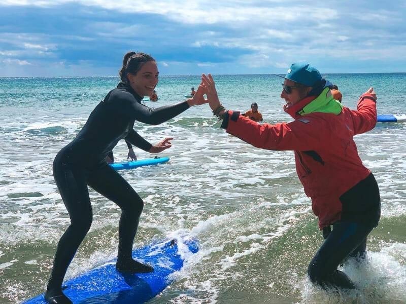 Une élève sur sa planche de surt et son moniteur faisant un high five dans l'eau