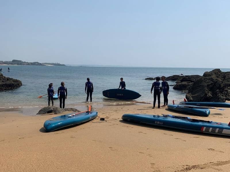 Des élèves et leur moniteur sur la plage, il y a également des planches de surf