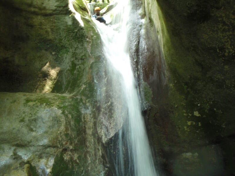 Personne en tenue de canyoning descendant une cascade d'eau dans un environnement rocheux et naturel.