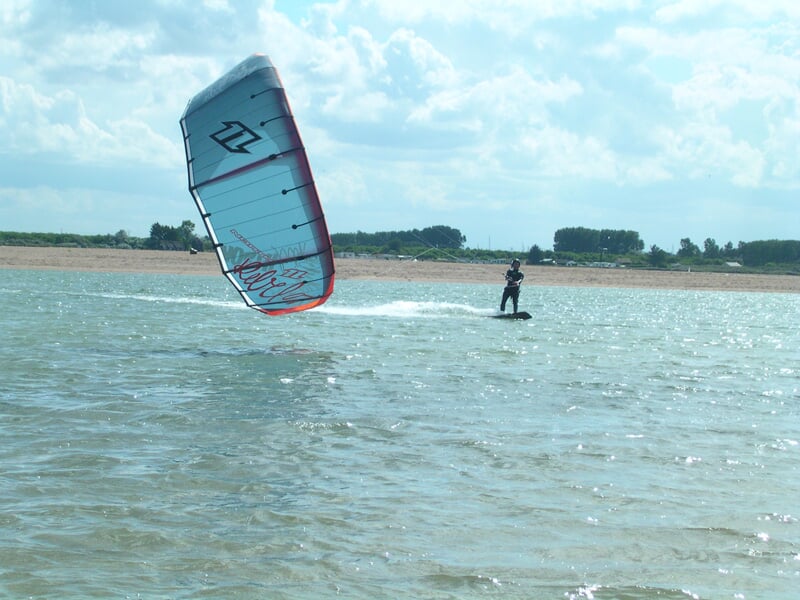 Un kitesurfeur navigue sur une étendue d'eau calme avec un grand cerf-volant bleu et rouge au-dessus.