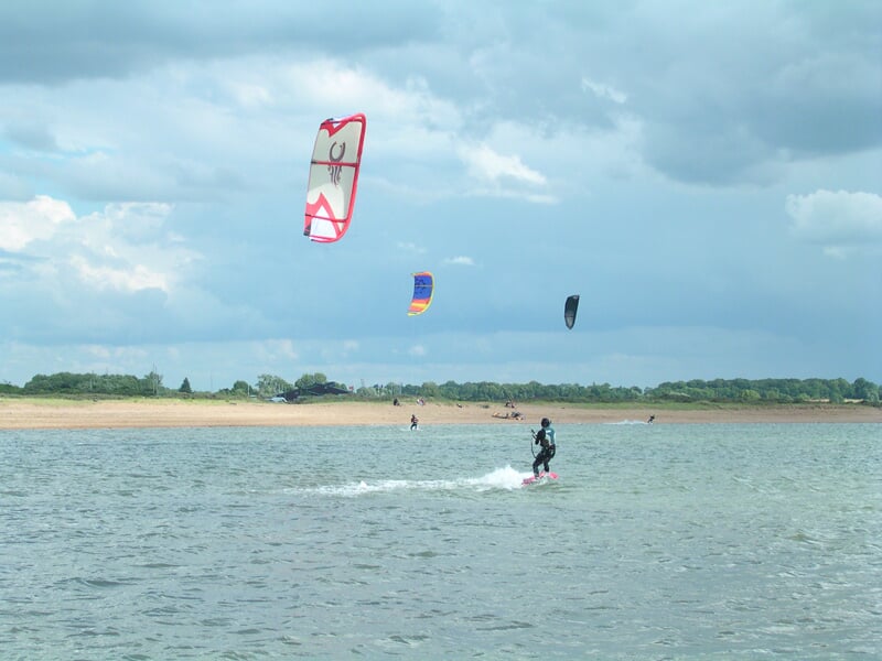 Plusieurs kitesurfeurs évoluent sur l'eau avec des cerfs-volants colorés sous un ciel nuageux.