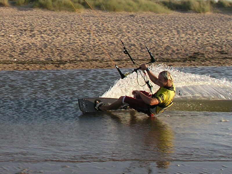 Un homme en tenue jaune pratique le kitesurf sur une étendue d'eau peu profonde près du sable.