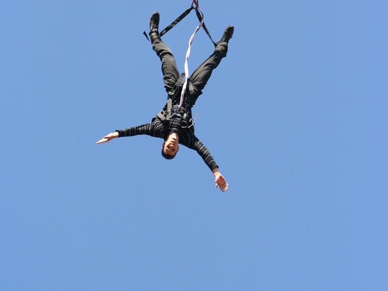 Personne en plein saut à l'élastique, suspendue la tête en bas dans un ciel bleu clair sans nuages.
