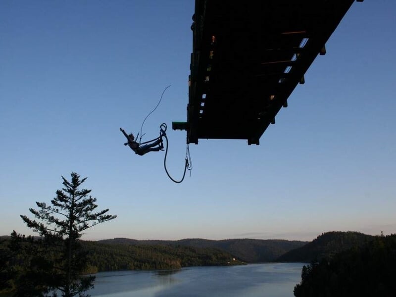 Saut à l'élastique depuis un pont suspendu au-dessus d'un lac entouré de collines boisées au coucher du soleil.