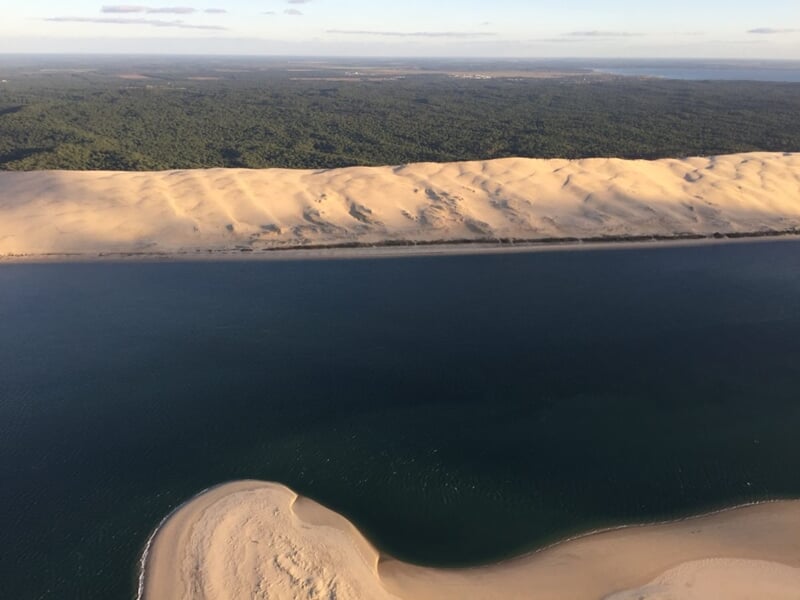 Dune du Pilat illuminée par la lumière du jour, longeant une étendue d’eau profonde et des bancs de sable isolés