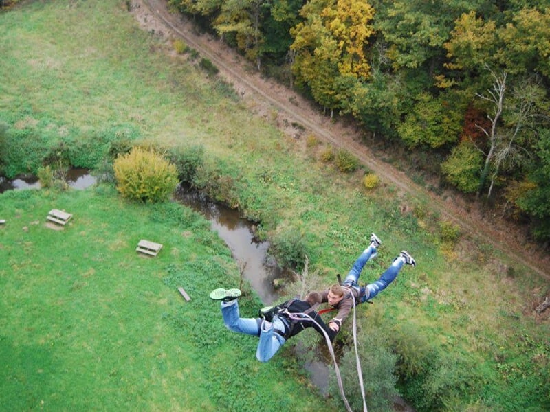 Personne effectuant un saut à l'élastique au-dessus d'un paysage vert avec arbres et rivière en contrebas.