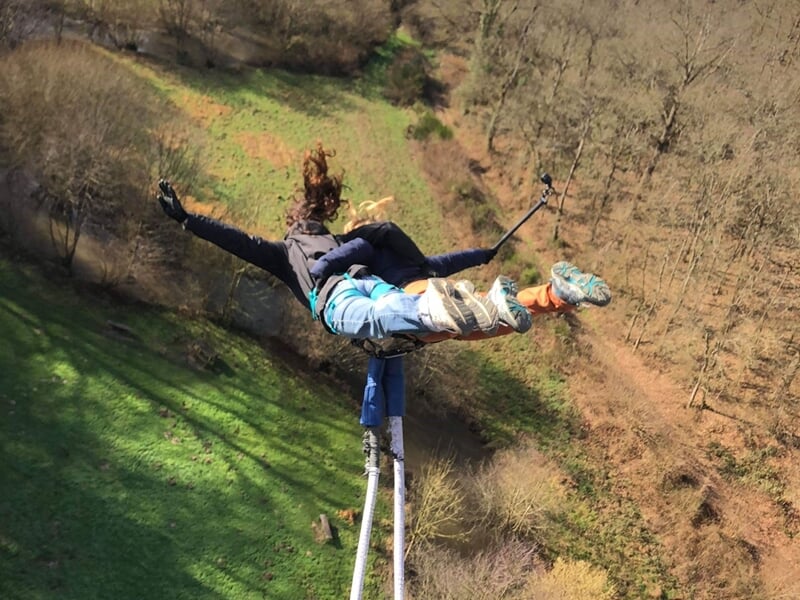 Saut à l'élastique d'une personne en tenue sportive, vue plongeante sur un paysage naturel avec arbres.