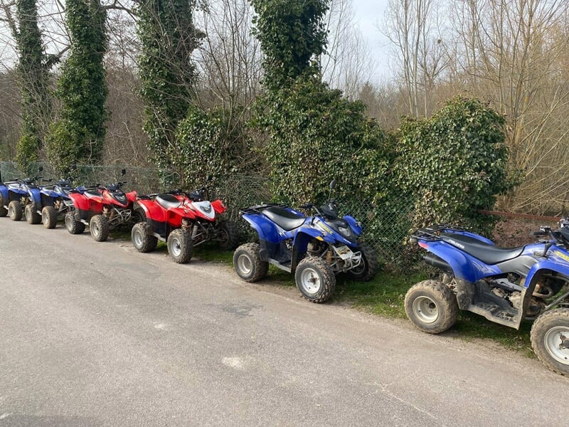 Une rangée de quads rouges et bleus garés le long d'une route bordée d'arbres et de buissons verts.