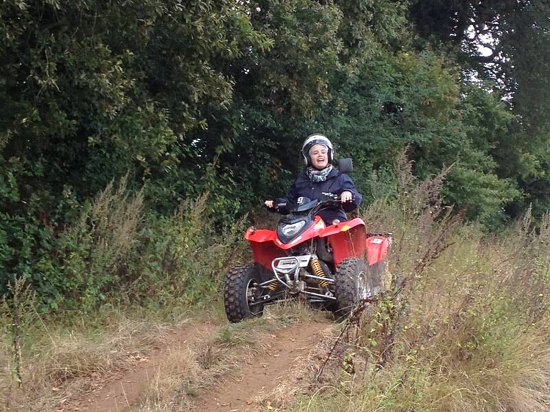 Personne en casque conduisant un quad rouge sur un chemin étroit entouré de végétation dense et verte.