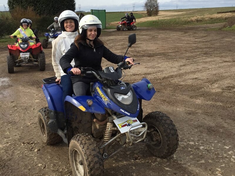 Groupe de personnes en casque sur des quads sur un terrain de terre, avec une femme souriante au premier plan.