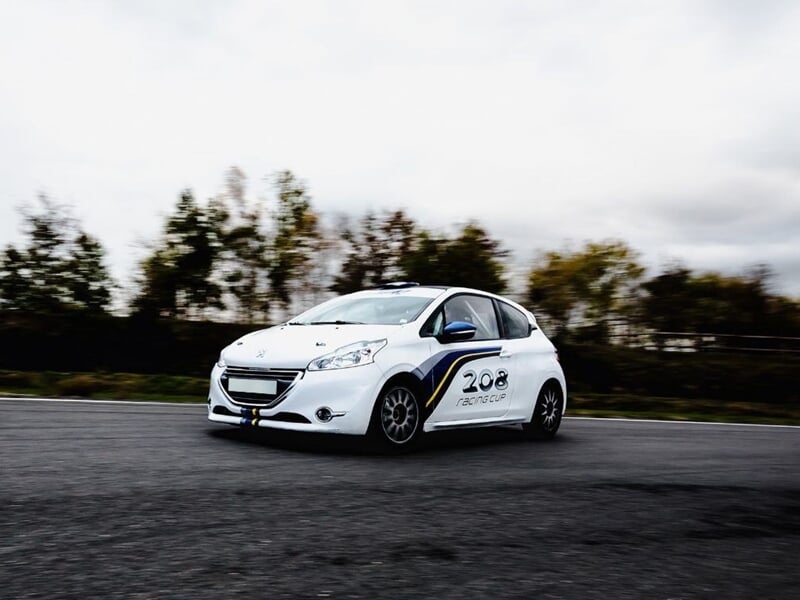 Voiture rouge de course sur circuit asphalte, prise de virage rapide avec pilotes à bord.