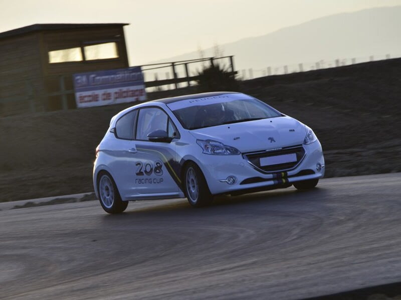 Voiture de course Peugeot 208 Racing Cup blanche en virage sur circuit asphalte lors d'un stage de pilotage rallye