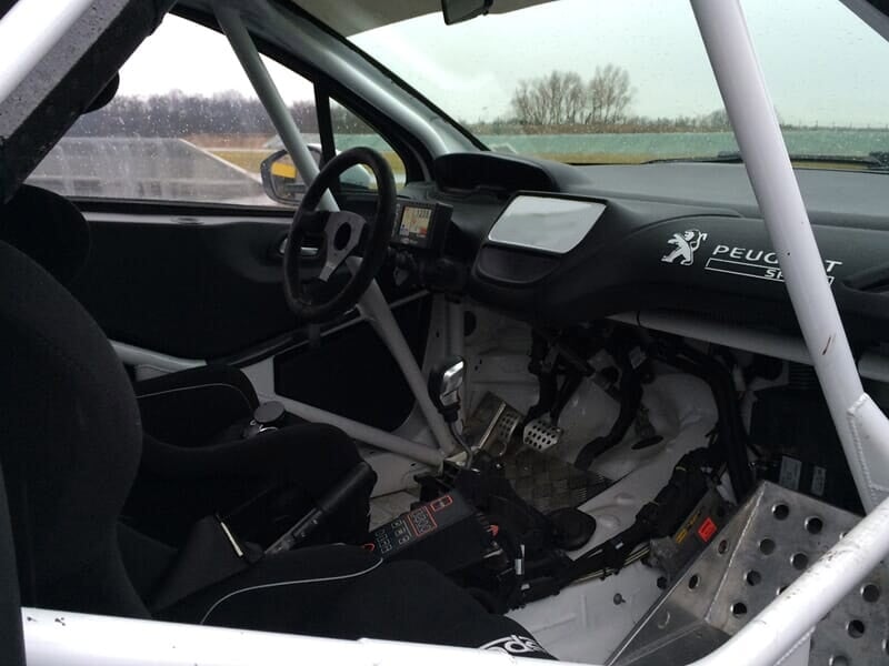 Voiture de course blanche avec passager, sur circuit asphalte, en pleine action.