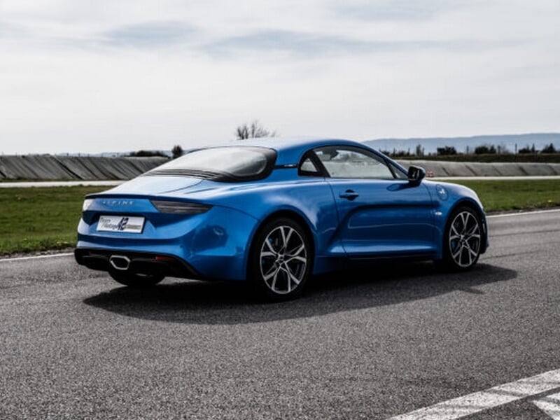 Alpine A110 bleue sur circuit asphalte, coaching pilotage avec pilote en pleine course.