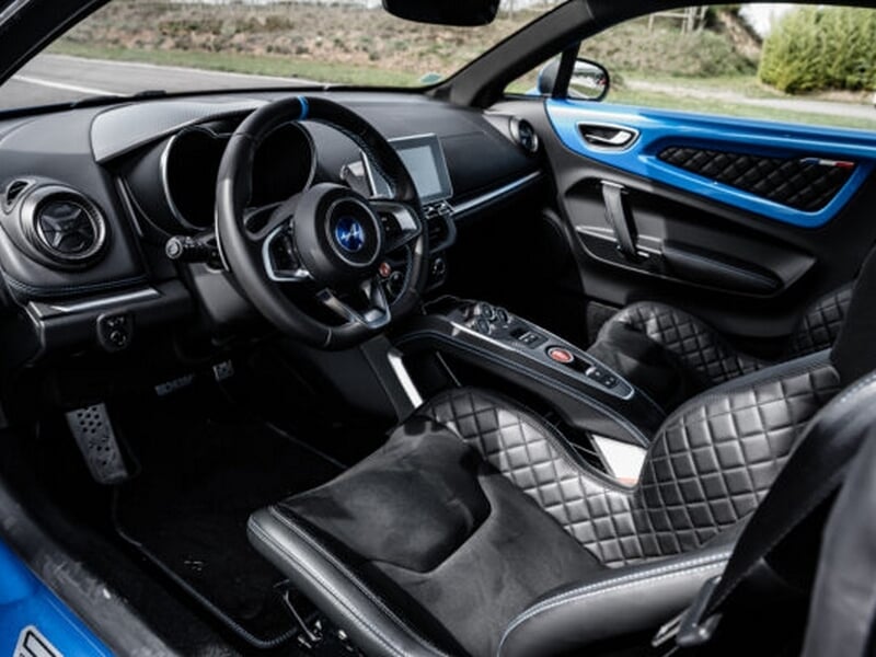 Intérieur d'une Alpine A110 avec volant, sièges en cuir matelassé et tableau de bord moderne bleu et noir.