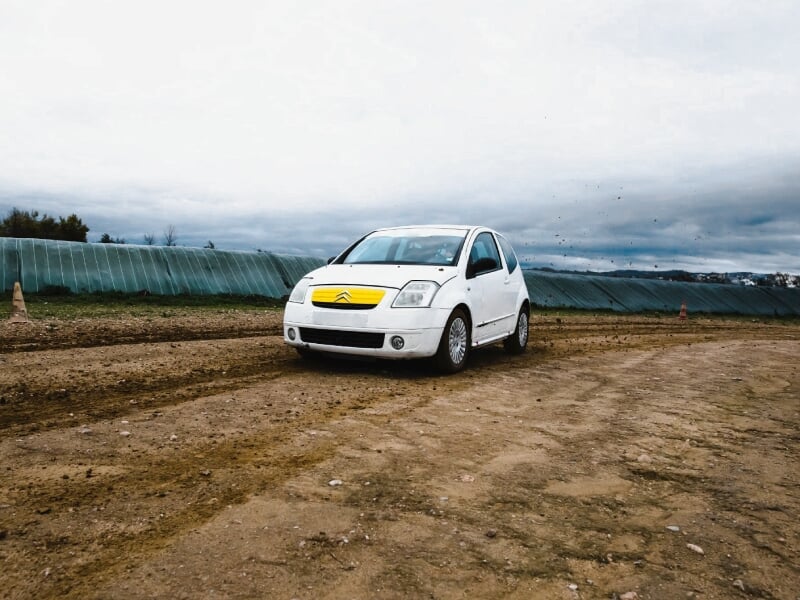 Voiture de rallye blanche sur circuit terre, en pleine action avec poussière visible.