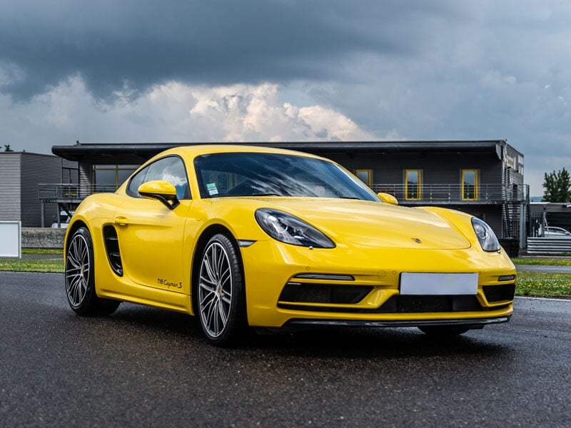 Porsche Cayman 718S sur circuit asphalte, coaching pilotage avec pilote casqué en pleine course.
